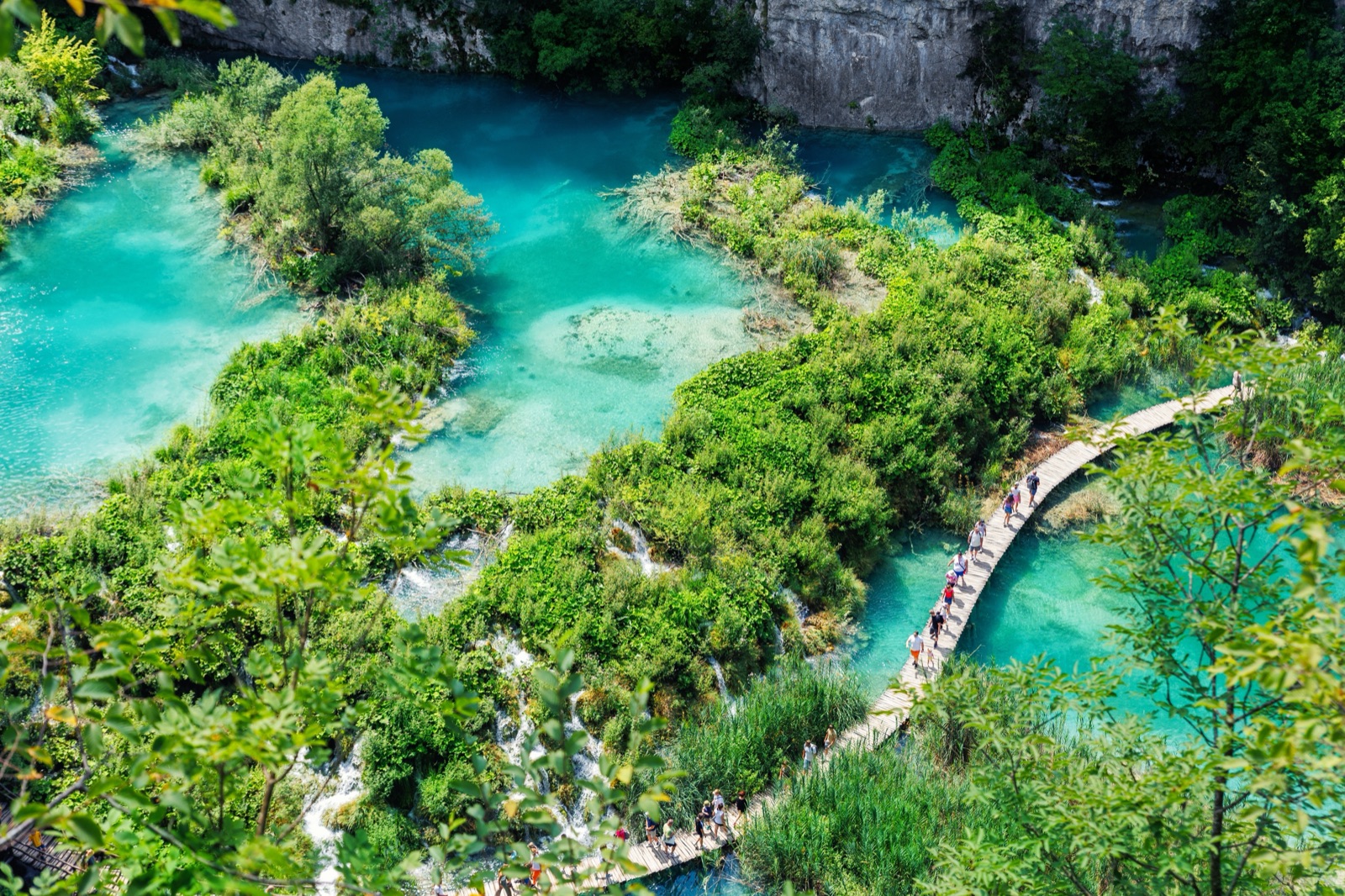 A wooden boardwalk crossing between turquoise pools at Plitvice